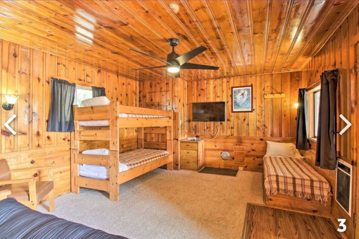 A wooden cabin room with bunk beds, a desk, a television, and a ceiling fan.