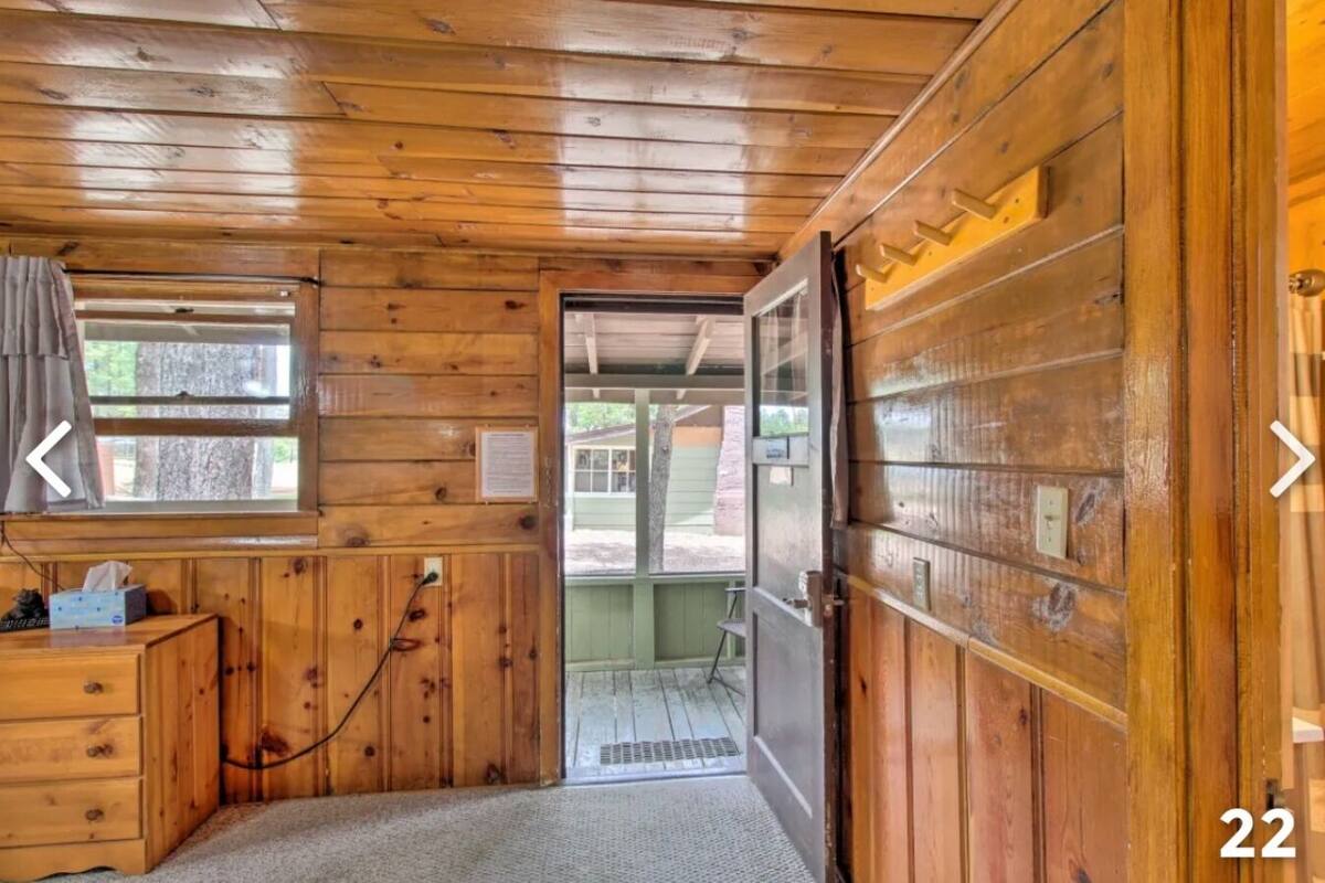 A wooden cabin interior with a wooden door, a window with curtains, a small wooden dresser, and a doorbell.
