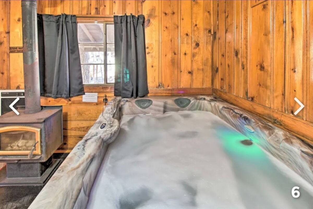 A wooden cabin interior with a hot tub, a wood-burning stove, and a window with curtains.