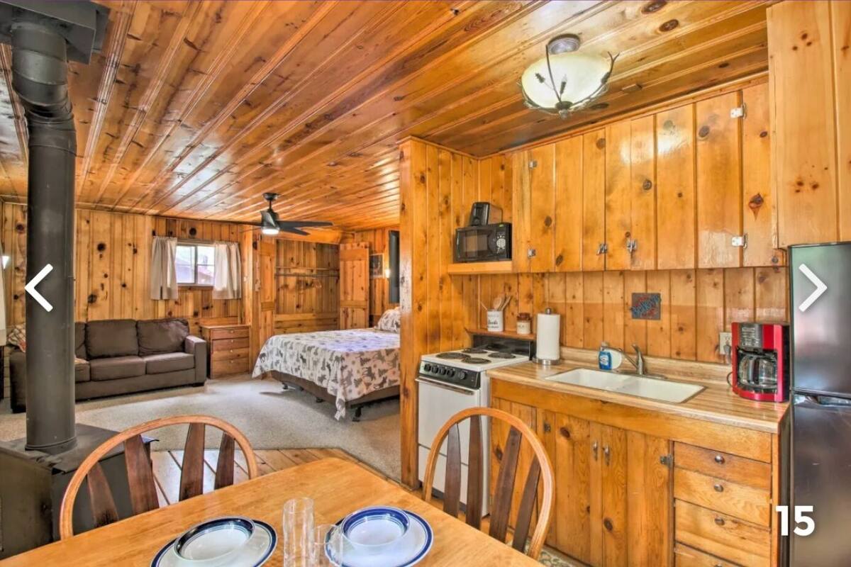A cabin interior with a wooden interior, a dining area with a table set for two, a kitchen with wooden cabinets, a stove, and a refrigerator.