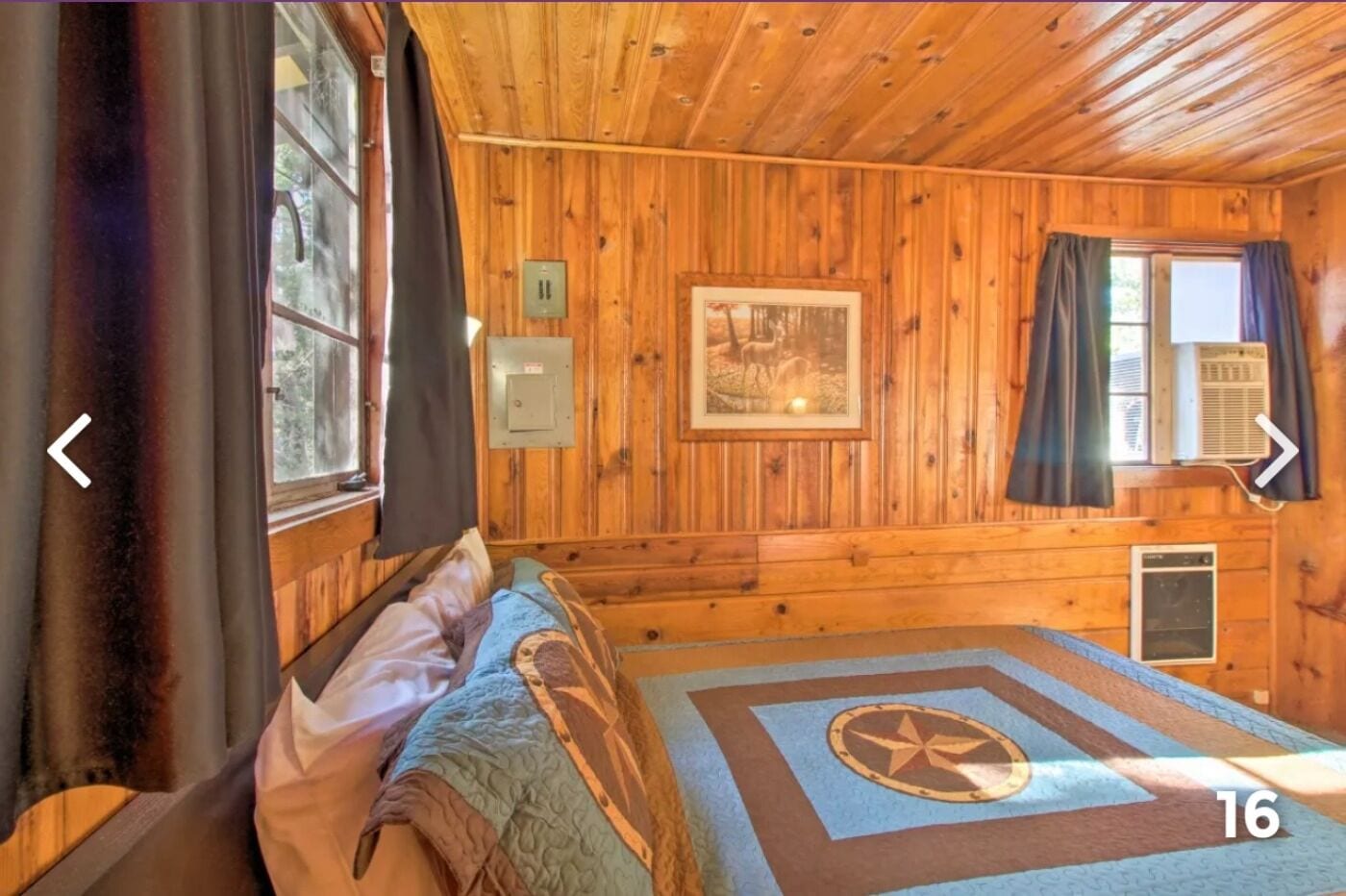 A cozy cabin room with a bed, a framed picture on the wall, and a window with curtains.