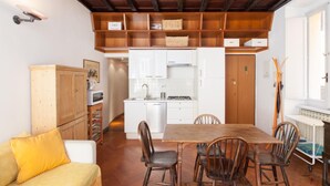 Cocina compacta con armarios blancos, una mesa de comedor con cuatro sillas y techo de madera.