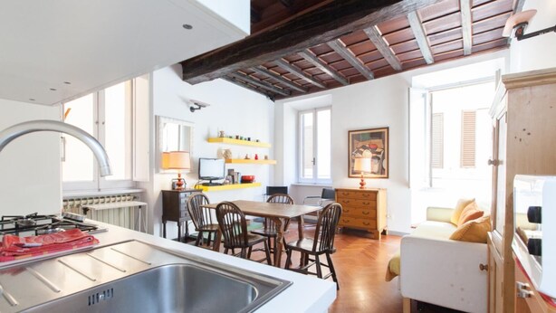 Una cocina moderna con una isla grande, un comedor con sillas de madera y una zona de estar acogedora con sofá y cojines.