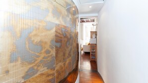 Un pasillo estrecho con una pared grande y decorada a la izquierda y un área de cocina visible a través de una puerta abierta a la derecha.