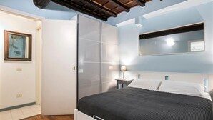 Un dormitorio con cama, armario, mesita de noche, lámpara y un cuadro en la pared.