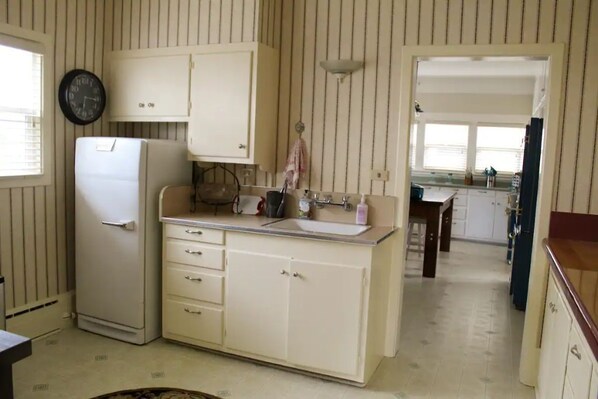 A kitchen with a refrigerator, sink, cabinets, and a clock on the wall. - 1919 Historic Craftsman Home (Scotia)
