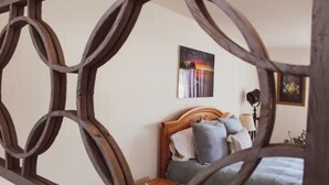 Een slaapkamer met een houten hoofdbord, een bed met meerdere kussens, een nachtkastje en een aan de muur hangend schilderij.