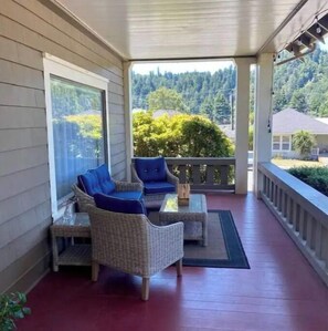 Relax on the covered porch with wicker furniture and enjoy the view of the surrounding forest and residential building.