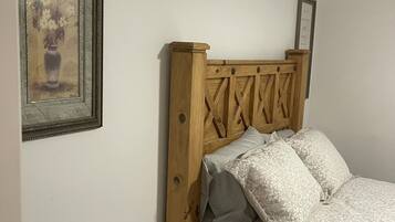 A bedroom with a wooden headboard, a bed with patterned bedding, a small round table, and a framed picture on the wall.