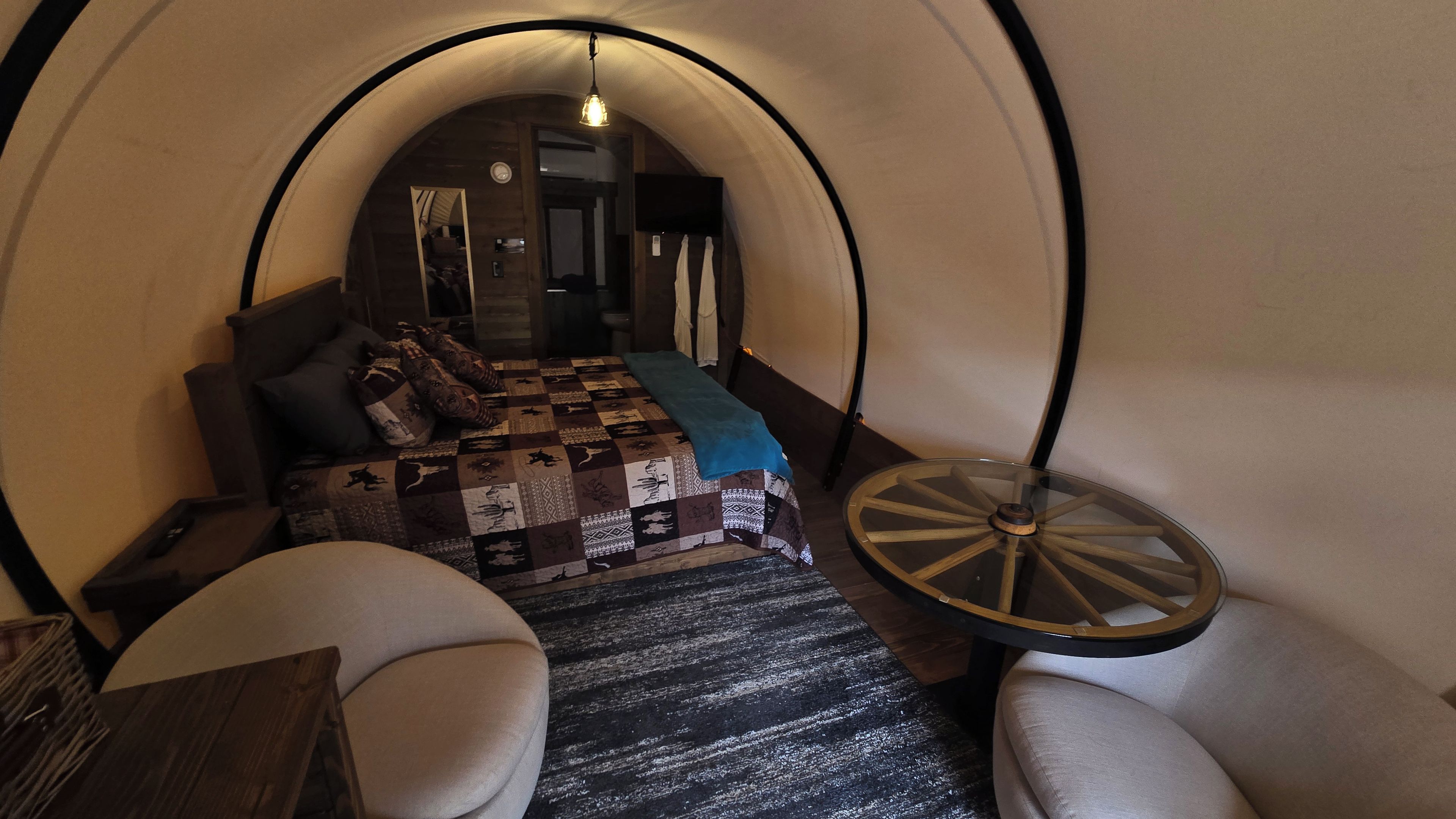 Quarto aconchegante e circular com uma cama, uma mesinha e duas cadeiras.