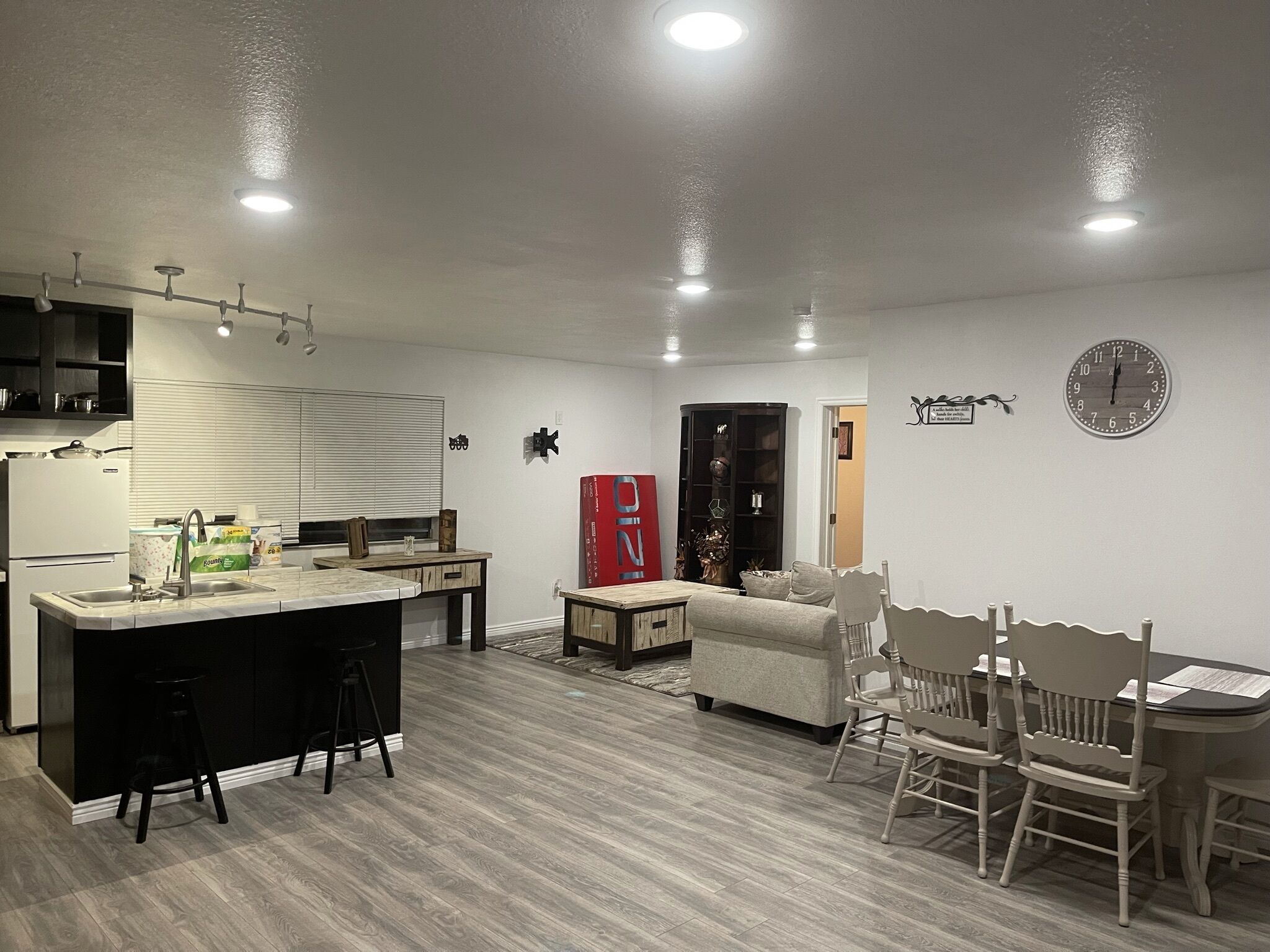 A modern kitchen with a central island, a dining area with a wooden table and chairs, and a living space with a sofa and a red cabinet.