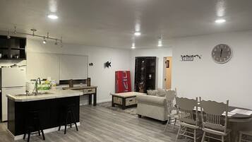 A modern kitchen with a central island, a dining area with a wooden table and chairs, and a living space with a sofa and a red cabinet.