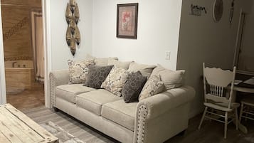 A living room with a beige sofa, patterned cushions, a wooden coffee table, and a rustic rug.