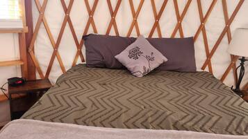 Una cama con colcha estampada, almohadas y manta en una habitación tipo tienda con pared de celosía de madera y un equipo de aire acondicionado.
