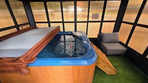 A hot tub with a wooden exterior and a blue interior, a wooden bench, and a gray sofa.