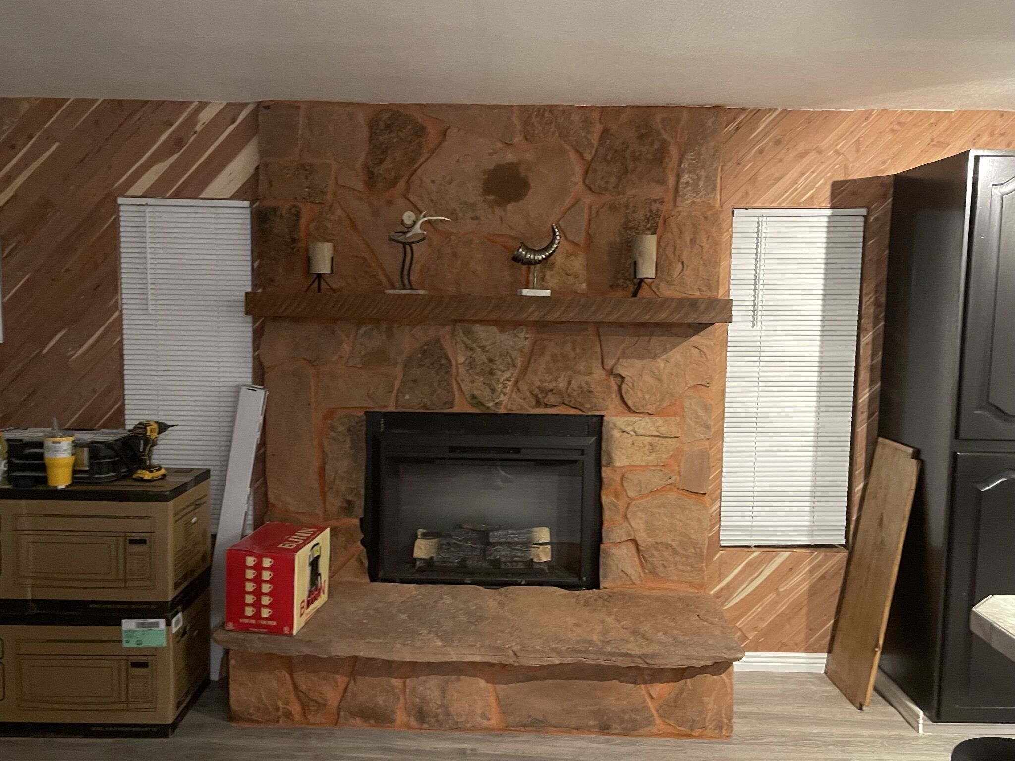 A stone fireplace with a mantel, flanked by wooden walls and white shutters.
