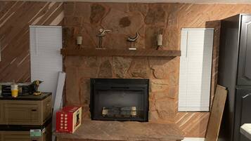 A stone fireplace with a mantel, flanked by wooden walls and white shutters.