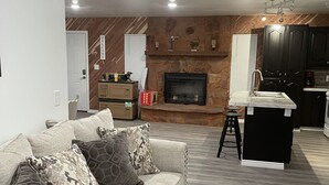 A living room with a sofa, a fireplace, a kitchen area, and a wooden accent wall. - Crazy Horse Rv Resort (Kanab)