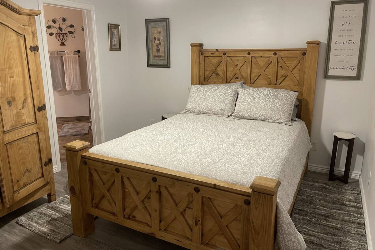 A bedroom with a wooden bed, a wooden wardrobe, a small rug, and a framed quote on the wall.