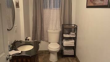 Un baño con tocador, lavamanos, espejo, inodoro y un perchero para toallas.
