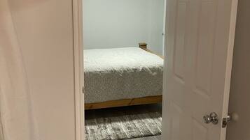 A narrow hallway leading to a bedroom with a bed, a ceiling fan, and an air conditioning unit.