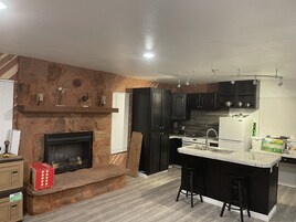 A modern kitchen with a stone fireplace, black cabinets, and a central island with stools.
