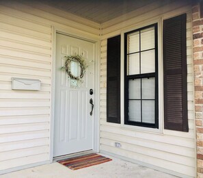 A white door with a doormat and a wreath, a mailbox, and two windows with shutters.