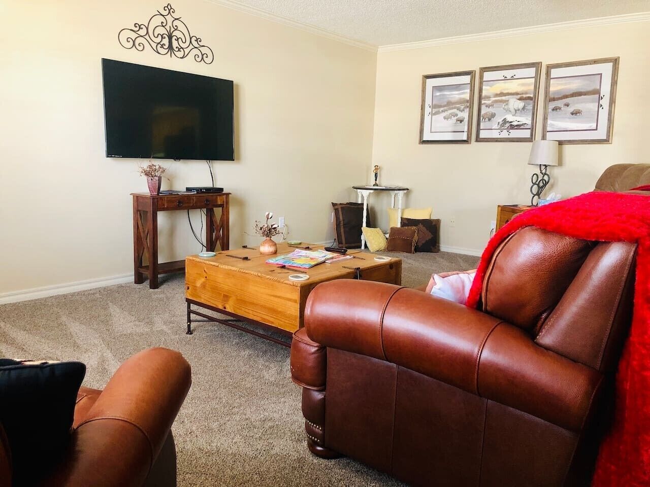 Un salon avec un canapé en cuir, une table basse, un téléviseur et des tableaux encadrés accrochés au mur.