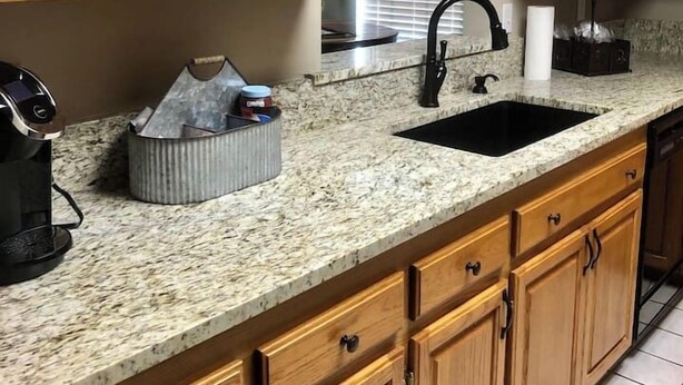 A kitchen with wooden cabinets, a granite countertop, a black sink, and a coffee maker.
