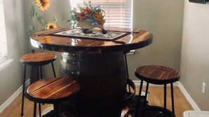 A bar area with a central wooden bar, two stools, a cowhide rug, and a hanging light fixture.