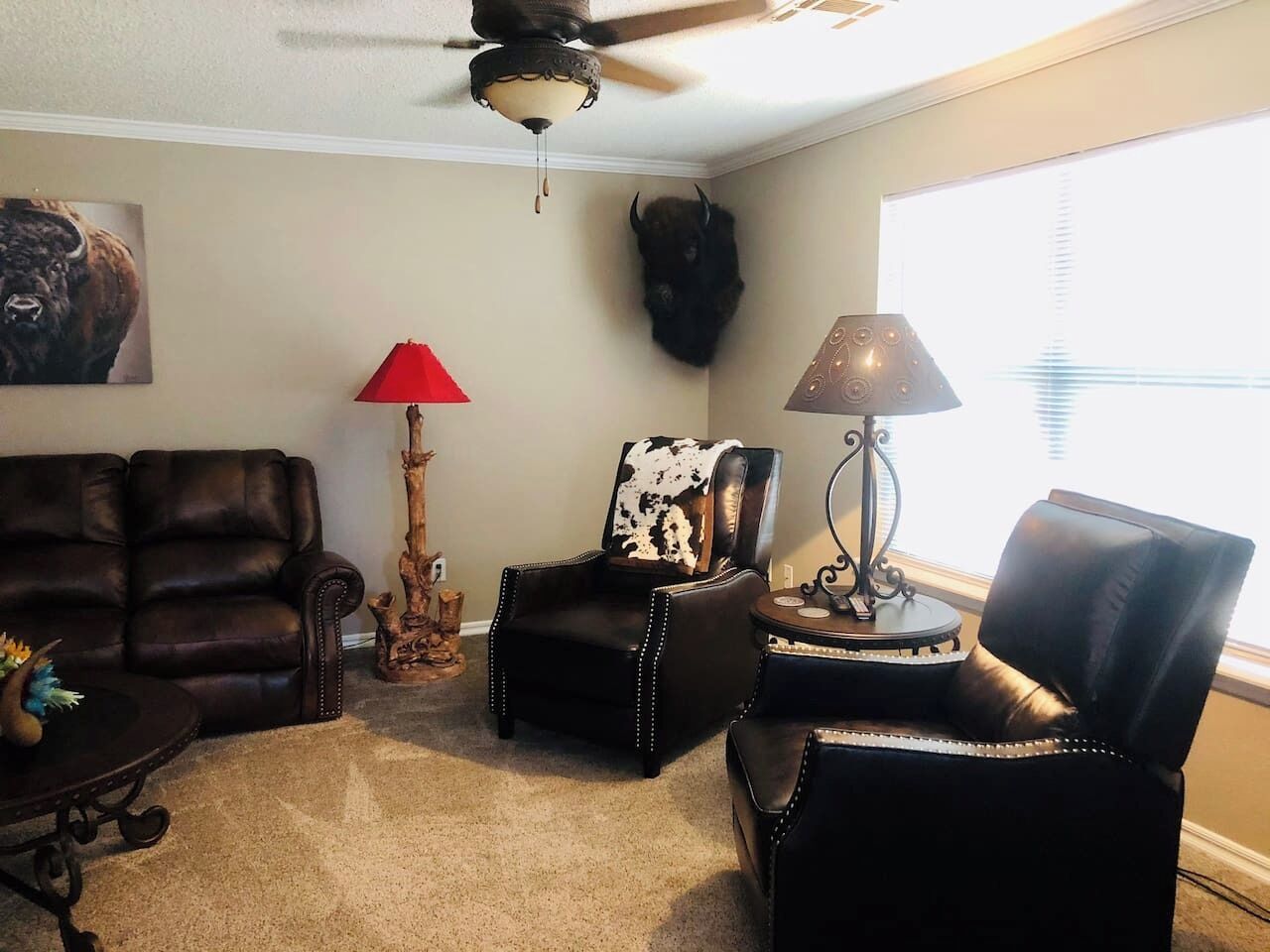 Un salon avec un ventilateur de plafond, un canapé, une table basse, une lampe et une tête d’animal fixée au mur.