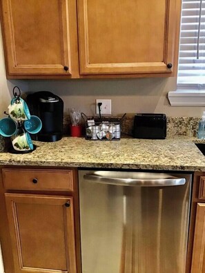A kitchen with wooden cabinets, a stainless steel dishwasher, and a granite countertop. - PIONEER VILLAGE-RED DIRT CABIN-3 BLOCKS TO MERC (Pawhuska)