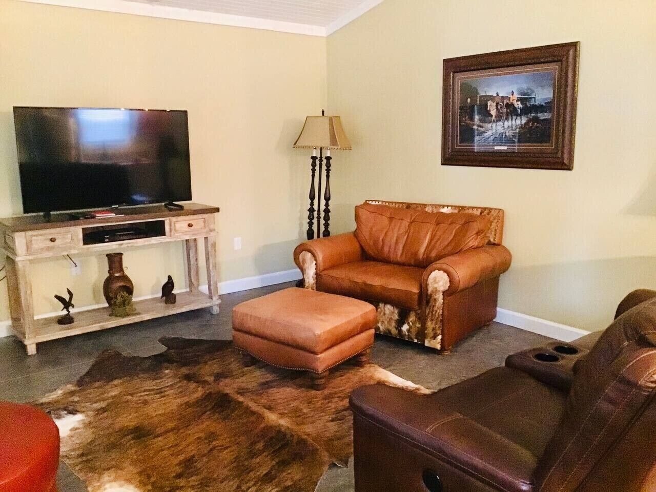 A living room with a television, leather sofa, ottoman, and a rug.