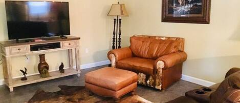 A living room with a television, leather sofa, ottoman, and a rug.