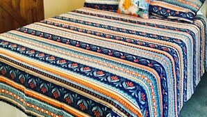 Una cama con una colcha estampada, un cabecero decorativo en la pared y una puerta de madera.
