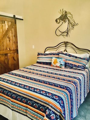 Ein Bett mit gemustertem Überwurf, einem dekorativen Wandvorhang als Kopfteil und einer Holztür.