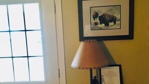 Una habitación con una puerta, una ventana, un cuadro en la pared, una lámpara y una pequeña mesa con un libro y un certificado.