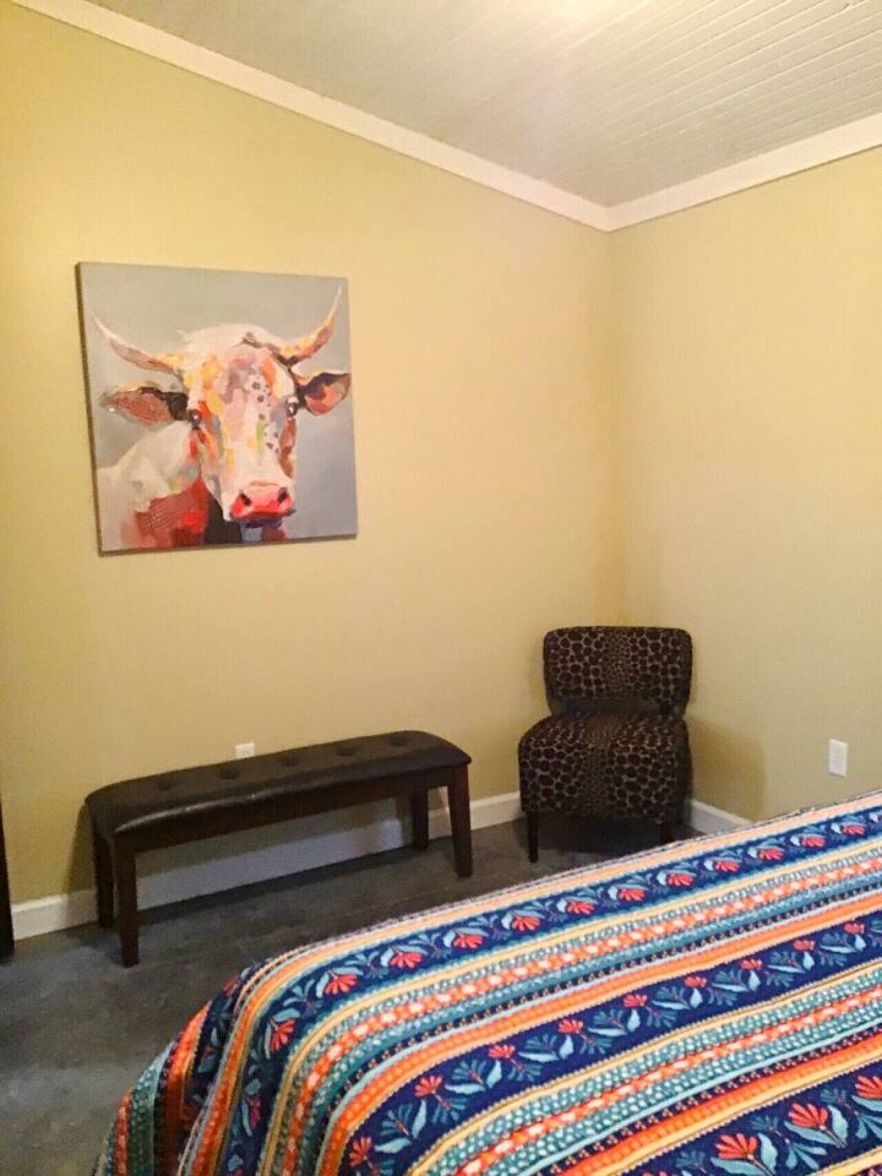 A bedroom with a bed, a bench, a chair, and a painting on the wall.