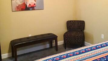 A bedroom with a bed, a bench, a chair, and a painting on the wall.