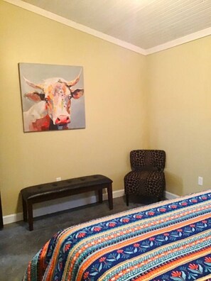 A bedroom with a bed, a bench, a chair, and a painting on the wall.