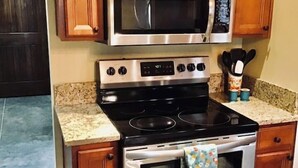 Una cocina con armarios de madera, un microondas de acero inoxidable, una estufa y un horno.