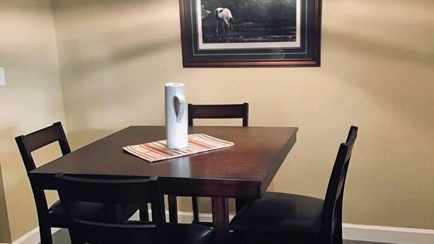 Un comedor con una mesa rectangular, cuatro sillas, una lámpara colgante y un cuadro en la pared.