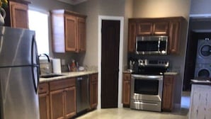 A kitchen with wooden cabinets, stainless steel appliances, and a tiled floor. - PIONEER VILLAGE-OKLAHOMA SKY CABIN-3 BLKS TO MERC (Pawhuska)