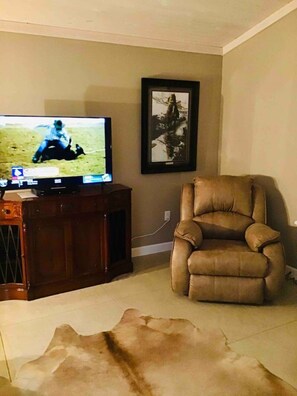 Ein Wohnzimmer mit Fernseher, einem gerahmten Bild an der Wand, einem Ledersessel und einem Teppich.