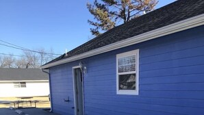 Un bâtiment bleu avec une porte et une fenêtre, un sol en béton et un ciel dégagé.
