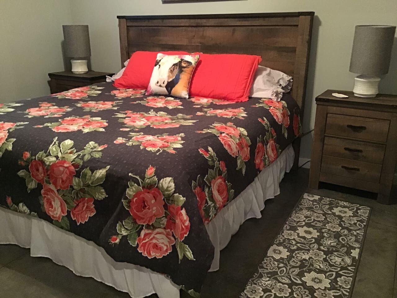 Un letto con una coperta a fiori, due cuscini, un comodino con una lampada e un tappeto decorato.