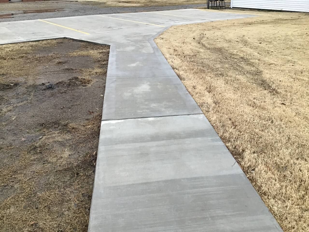 Un sendero de concreto que lleva a una zona verde con un edificio al fondo.