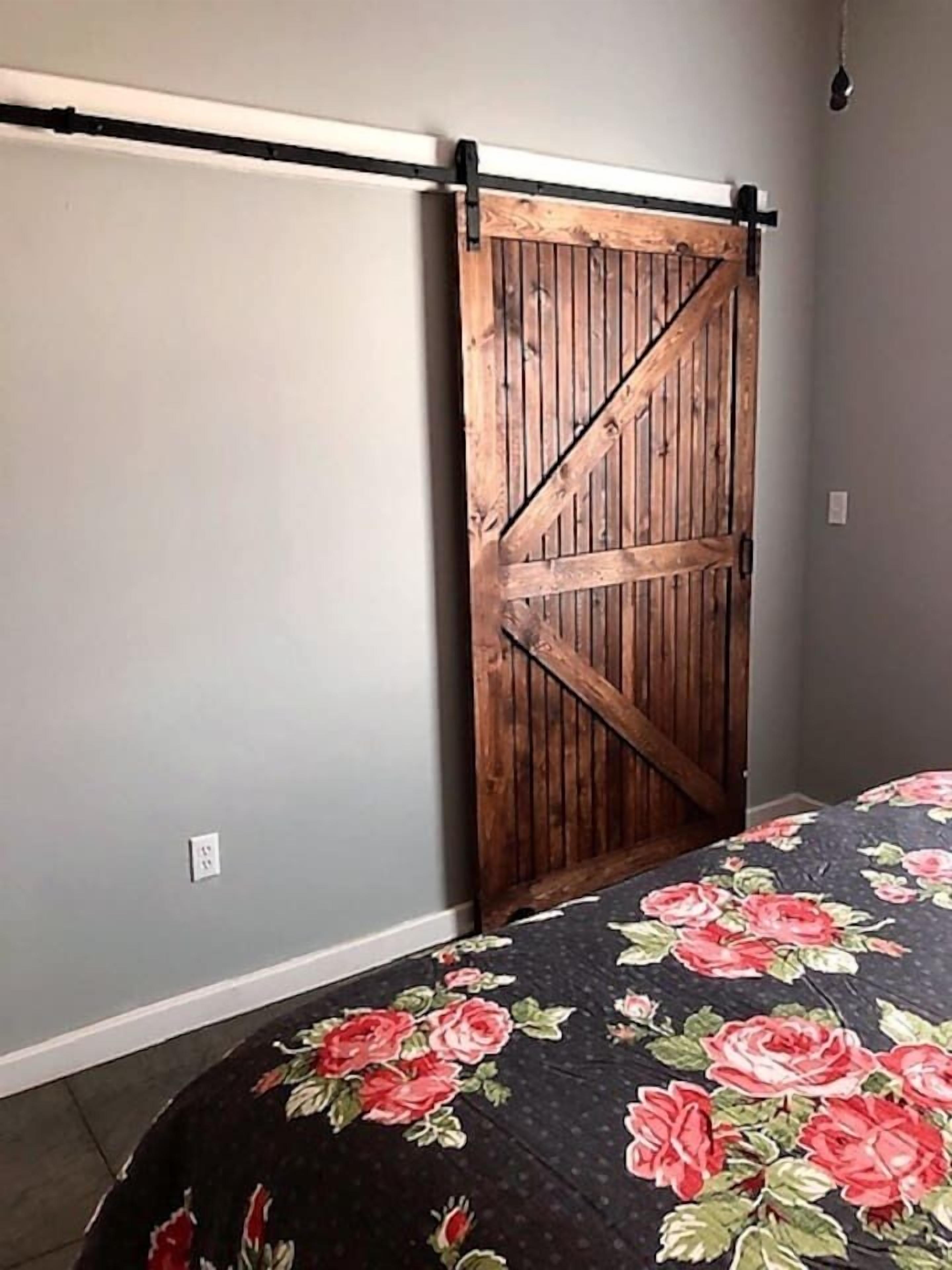 Una habitació amb una porta corredissa de tipus graner, un llit amb colcha floral i un interruptor a la paret.