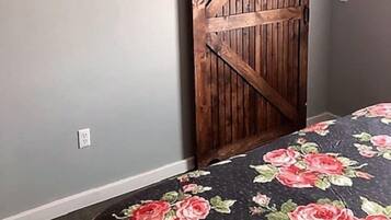 Una habitació amb una porta corredissa de tipus graner, un llit amb colcha floral i un interruptor a la paret.