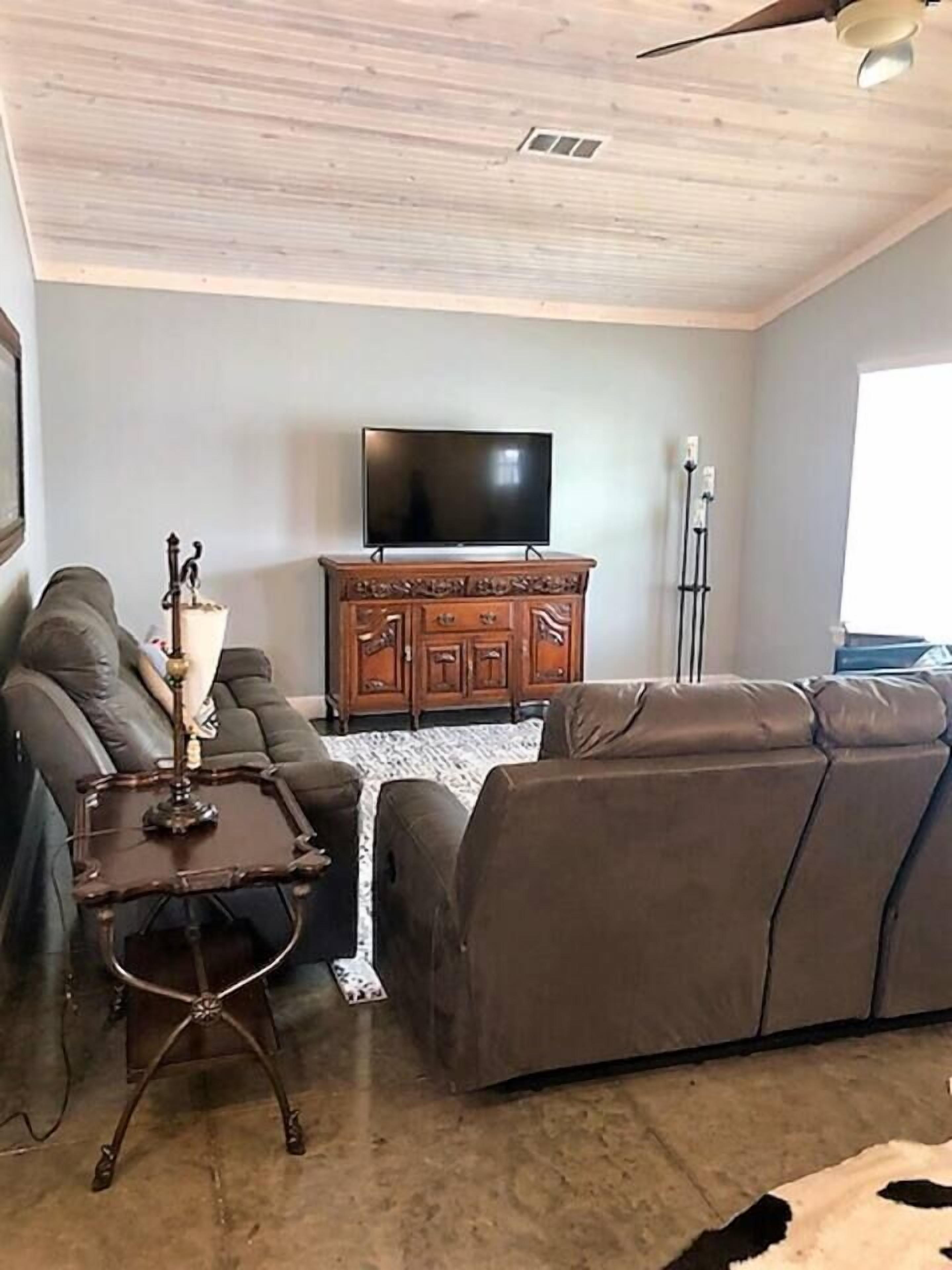 A living room with a brown leather sofa, a wooden cabinet, a flat-screen TV, and a ceiling fan.
